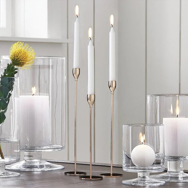 A set of tall white candles in brass holders displayed on a wooden surface.