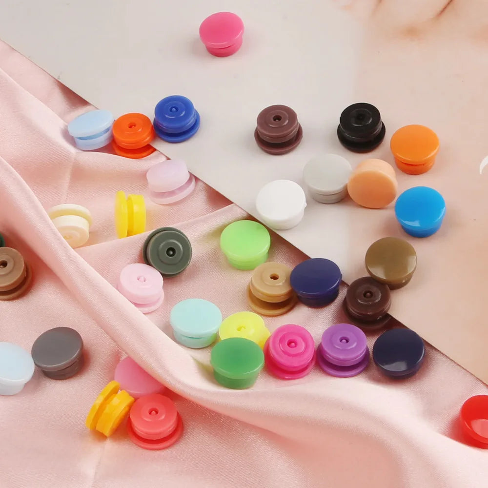 Assorted snap buttons in various colors like pink, blue, orange, and black are arranged on pink fabric.