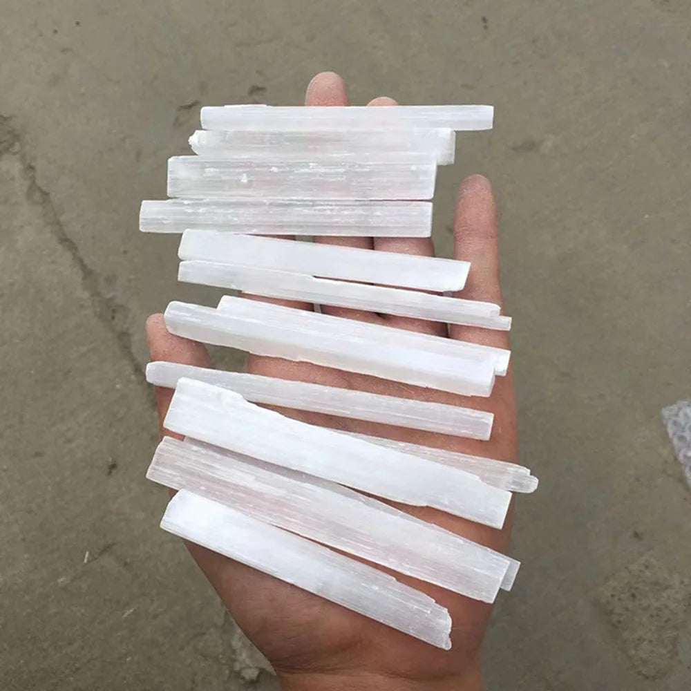 A hand holds several translucent white selenite crystal wands arranged in a fan shape.