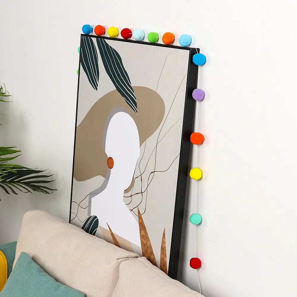 A vertical piece of art featuring a silhouette of a woman and abstract lines, decorated with a colorful felt ball garland.