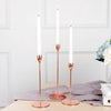 Three tall, slender copper-toned candles in glass holders standing on a wooden surface.