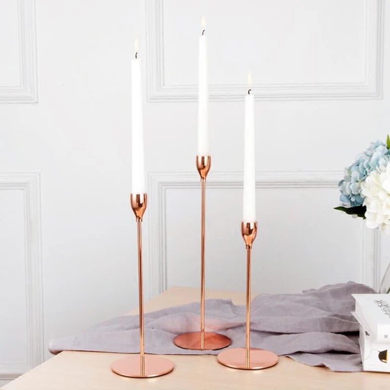 Three tall, slender copper-toned candles in glass holders standing on a wooden surface.