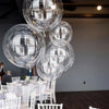 Clear spherical balloons reflecting light are suspended in the air above a white table setting.