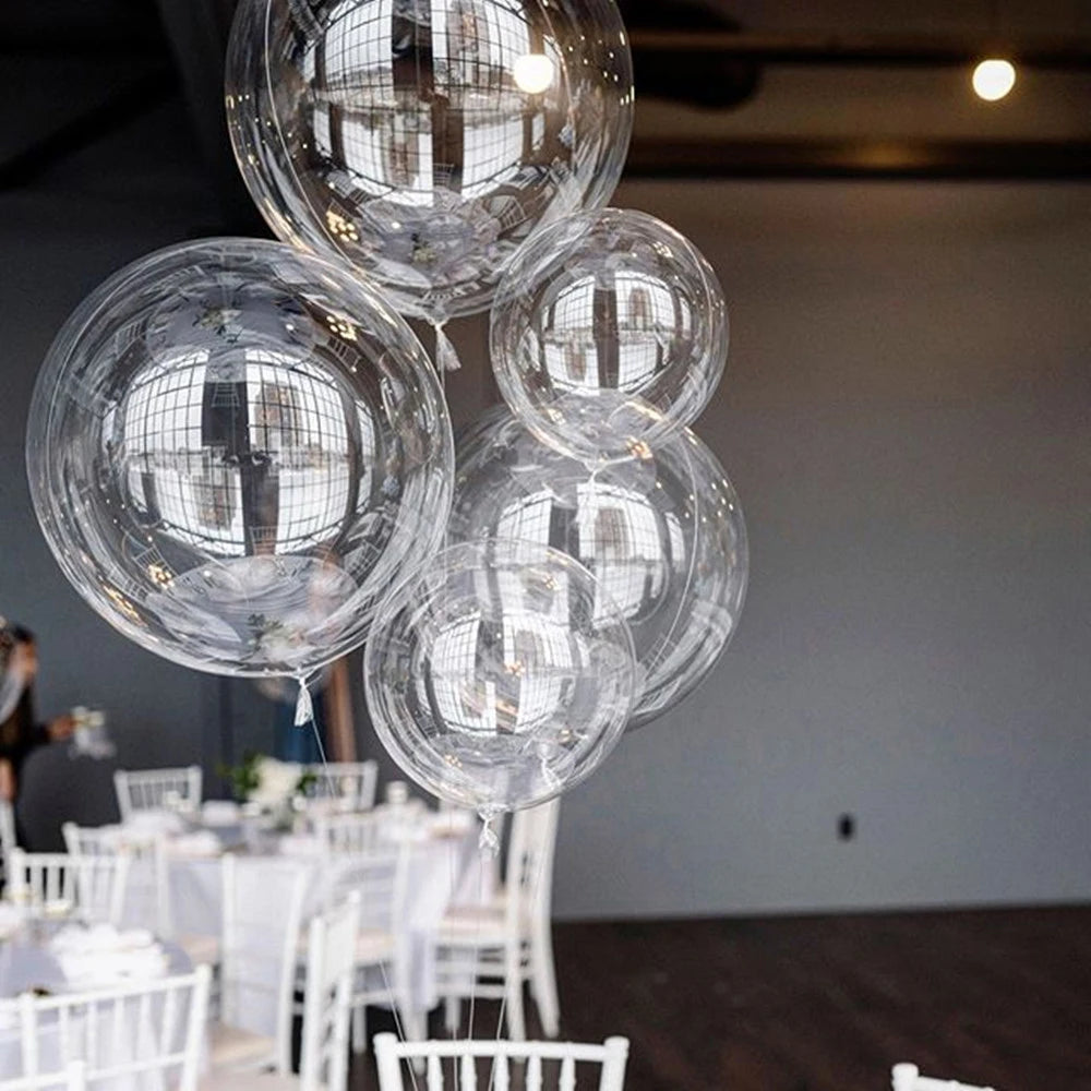 Clear spherical balloons reflecting light are suspended in the air above a white table setting.