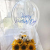 A clear balloon arch featuring blue script that reads Happy Mother's Day surrounded by a bouquet of yellow sunflowers.