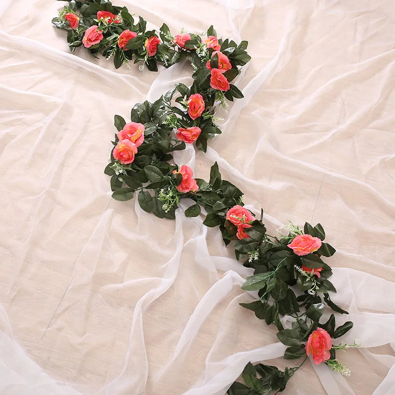 A green silk rose hanging vine garland with pink and orange roses laid on sheer white fabric.