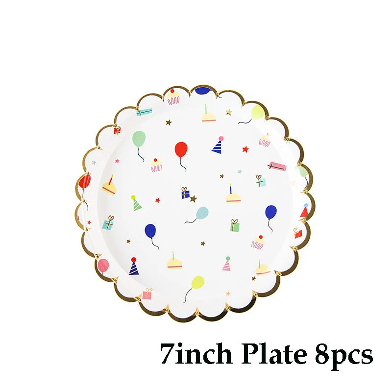 A white disposable paper plate with a gold rim decorated with colorful cartoon party icons like balloons and cupcakes.