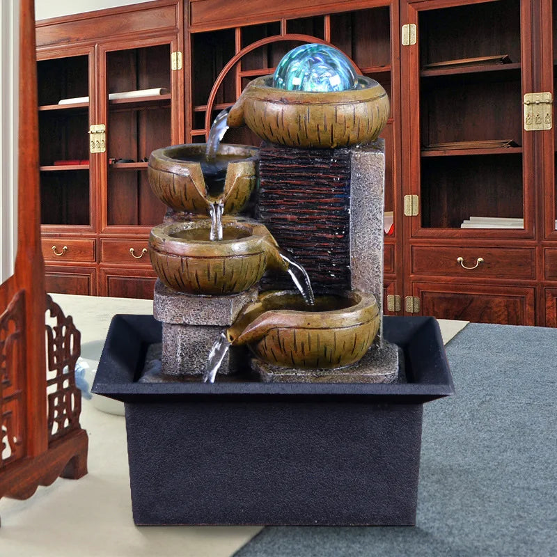 A tabletop water fountain featuring stacked ceramic bowls and a glowing orb, set in a dark rectangular base.