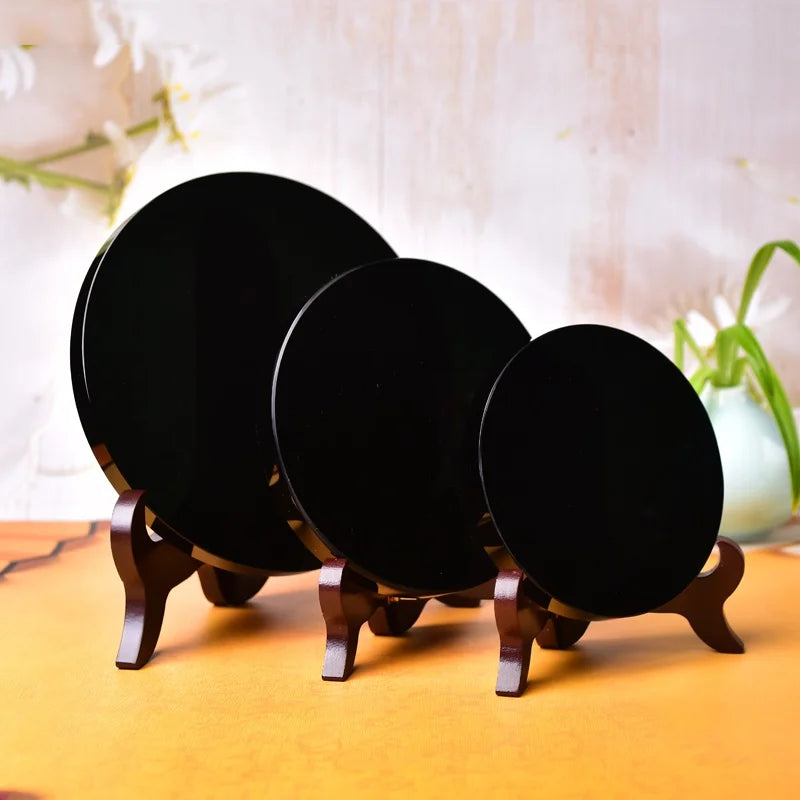 Three round black obsidian mirrors displayed on wooden stands.