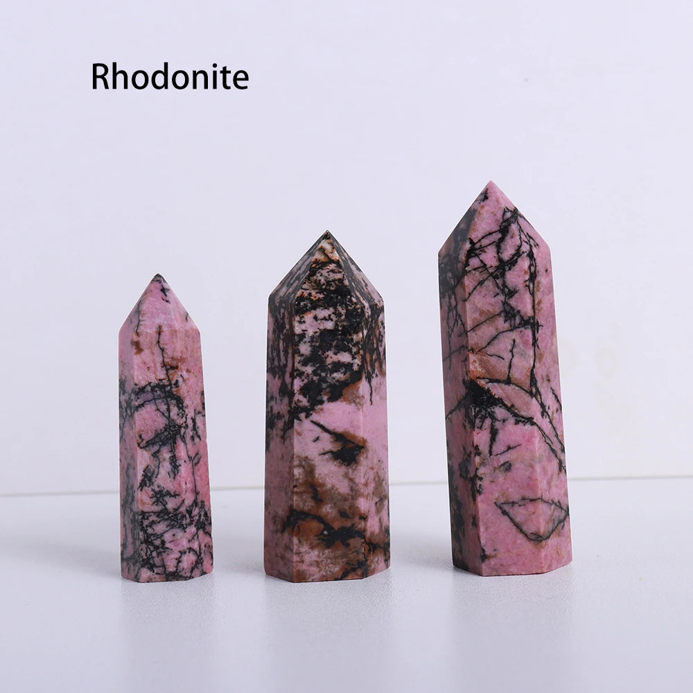 A vertical pink and black Rhodonite crystal point prism tower displayed on a white surface.