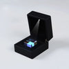 A black box with an open lid displaying a blue iridescent optical glass prism cube.