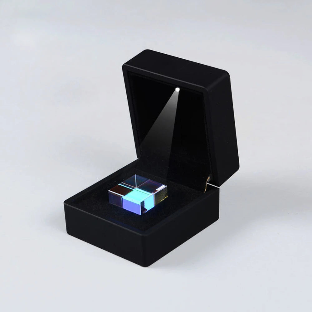 A black box with an open lid displaying a blue iridescent optical glass prism cube.