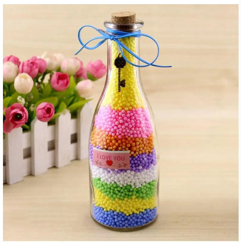 A glass bottle filled with colorful pastel foam beads arranged in horizontal stripes, tied with blue string and topped with a