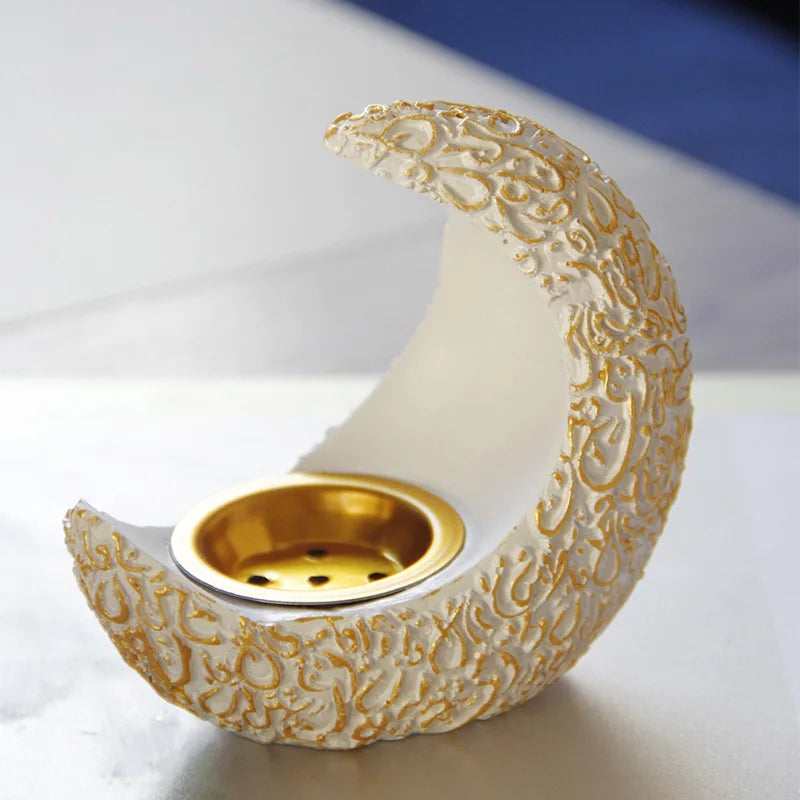 An antique crescent resin incense burner with a textured white body and gold accents sits on a light surface.