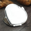 A small silver heart-shaped folding makeup mirror is shown on a dark wooden surface.