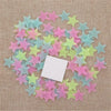 A collection of 50 glow-in-the-dark star wall stickers in various pastel colors scattered on a beige fabric background.