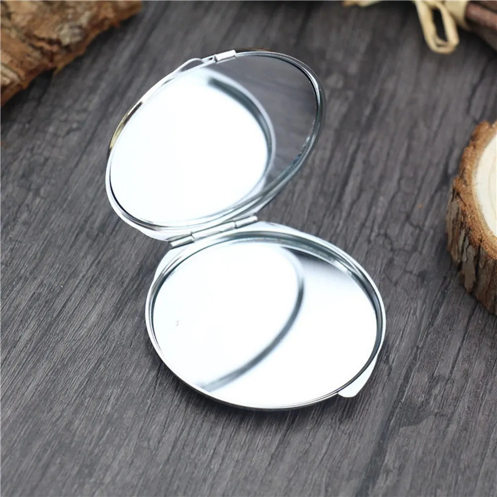 A silver mini double-sided folding makeup mirror is shown open on a dark wooden surface.