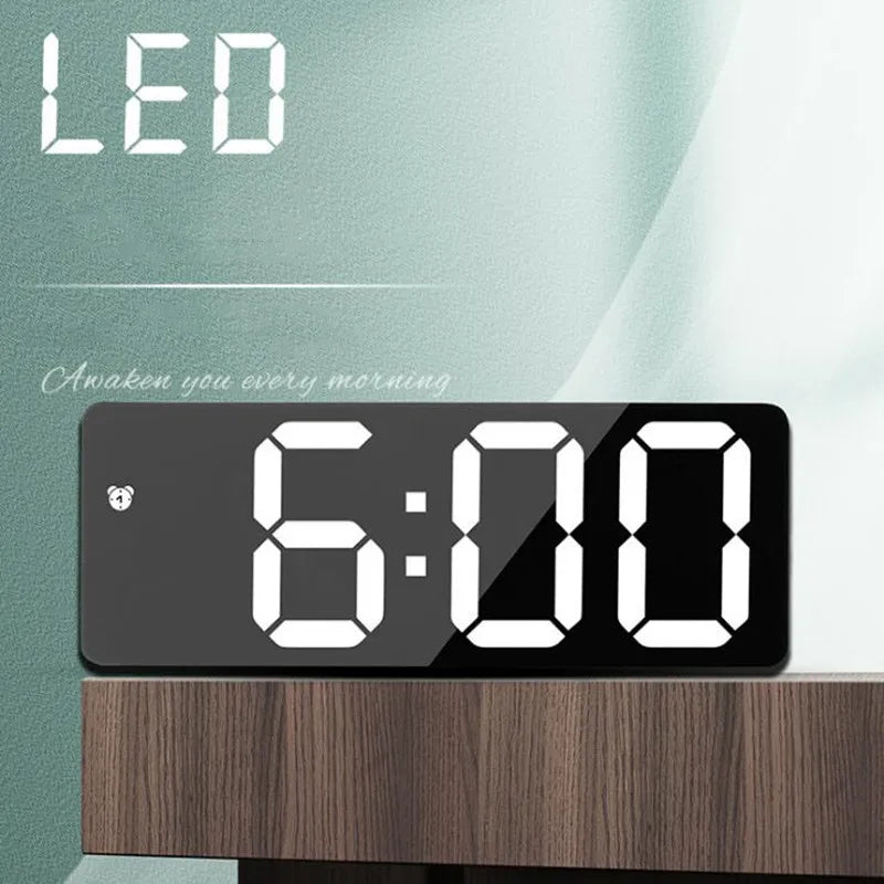 A black LED digital alarm clock displaying 6:00 on a wooden surface.