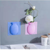 A pink ceramic flower vase is mounted on a gray wall, next to a blue vase, against a light gray background.