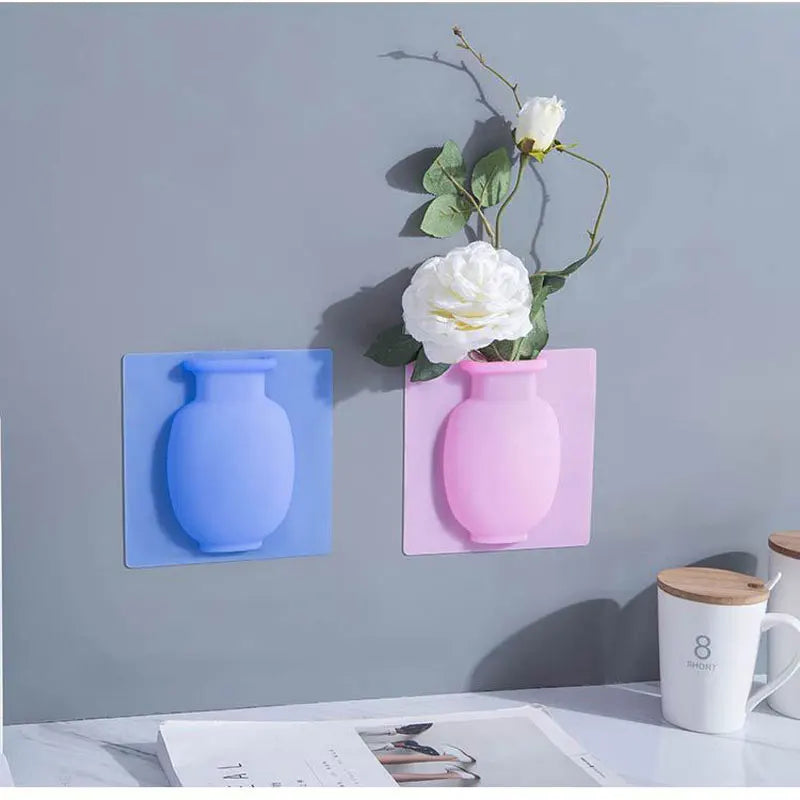 A pink ceramic flower vase is mounted on a gray wall, next to a blue vase, against a light gray background.
