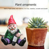 A ceramic gnome statue with a red hat and green outfit sits next to a potted succulent plant.