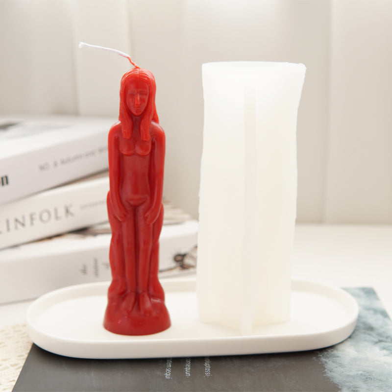 A red silicone mold shaped like a realistic human figure stands next to a white pillar candle.