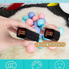 A hand holds a digital device measuring liquid, surrounded by colorful plastic balls on a white fluffy surface.