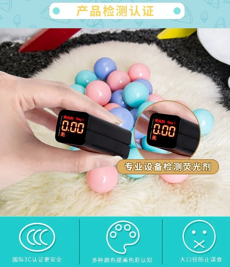 A hand holds a digital device measuring liquid, surrounded by colorful plastic balls on a white fluffy surface.
