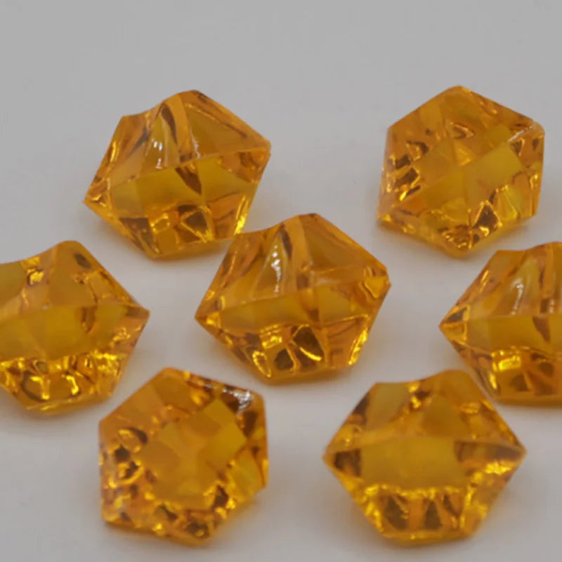 Several faceted yellow acrylic crystal decorations for parties scattered on a white surface.