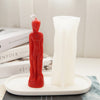 A red silicone mold shaped like a realistic human figure stands next to a white candle mold on a white tray.