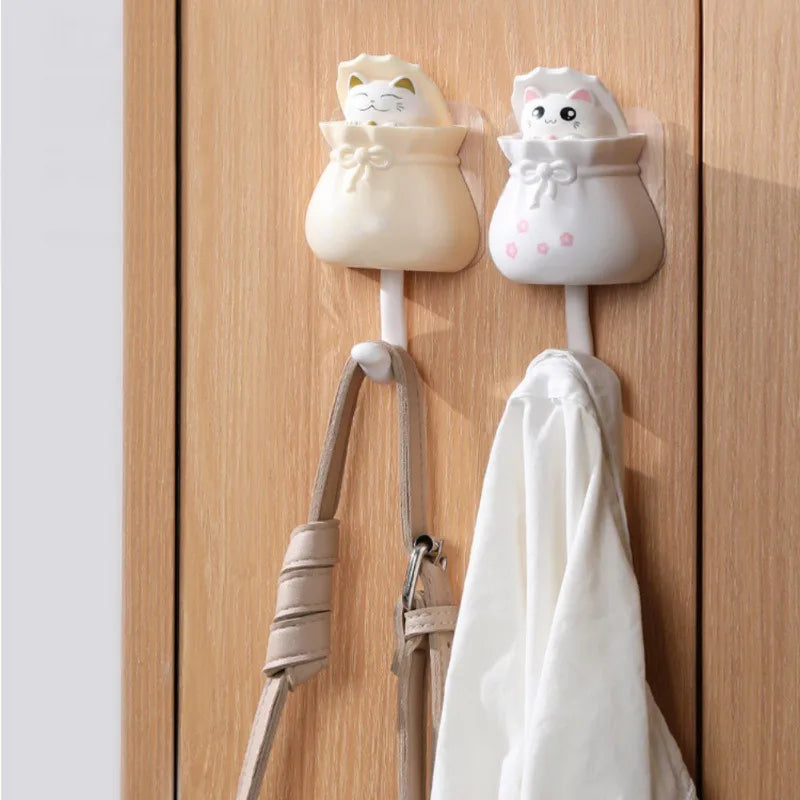 Two white cartoon cat wall hooks with fabric loops hanging on a wooden cabinet door.