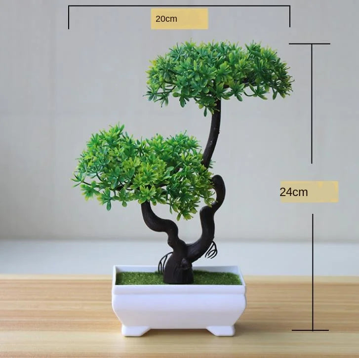 Artificial bonsai tree with green foliage displayed in a white rectangular pot on a wooden surface.