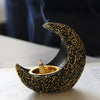 A black crescent moon shaped resin incense burner with gold detailing and a wooden stick emitting smoke.