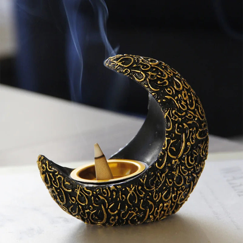 A black crescent moon shaped resin incense burner with gold detailing and a wooden stick emitting smoke.