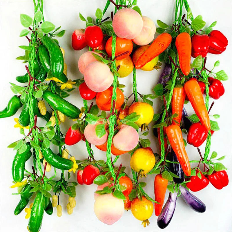 A vibrant arrangement of lifelike artificial fruits and vegetables including tomatoes, carrots, and peppers on a green vine.