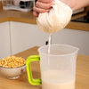 A hand pours a thick white liquid from a fine mesh bag into a clear jug.