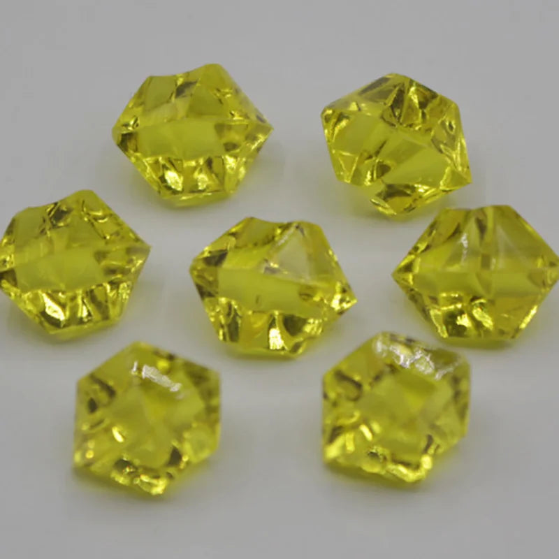 A collection of yellow acrylic crystal decorations shaped like pyramids and cubes for parties.