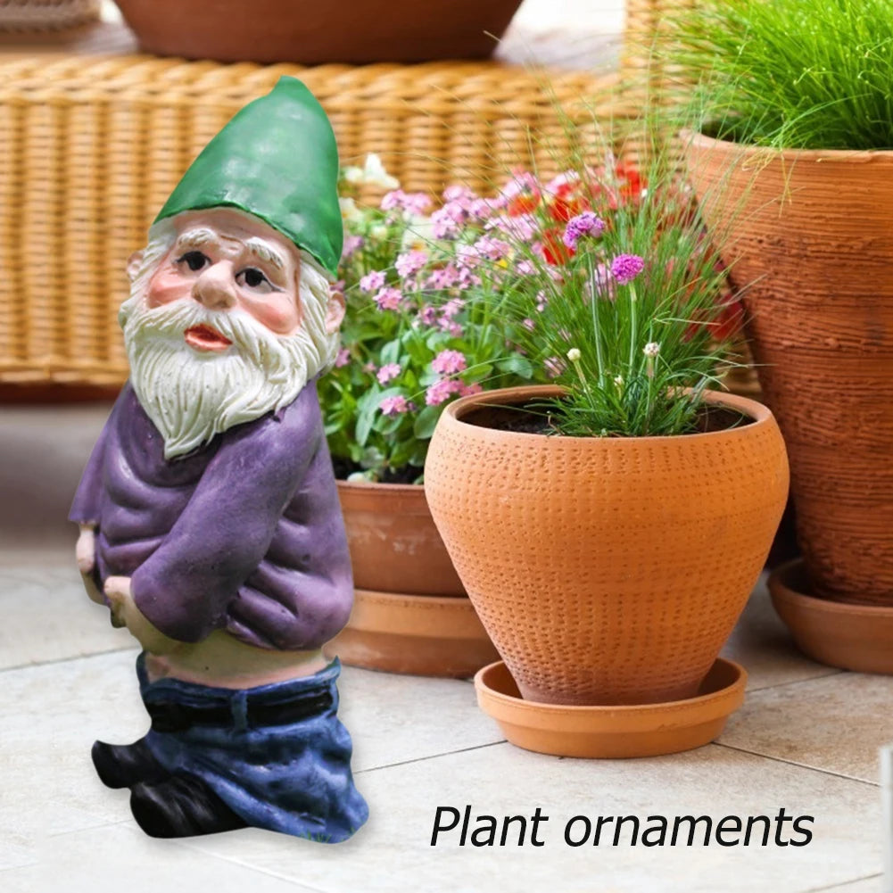 A miniature resin gnome statue with a green hat and purple clothing standing next to potted flowers.