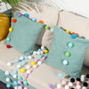 A pastel colored felt ball garland featuring various shades of blue, green, yellow, and pink strung across a light-colored so