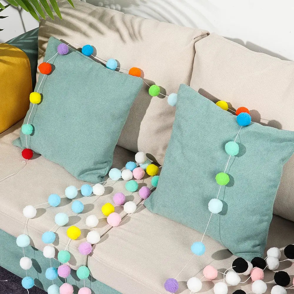 A pastel colored felt ball garland featuring various shades of blue, green, yellow, and pink strung across a light-colored so