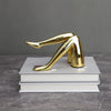 A gold faux finish sculpture of a human leg, cast in resin and displayed on a stack of white books.
