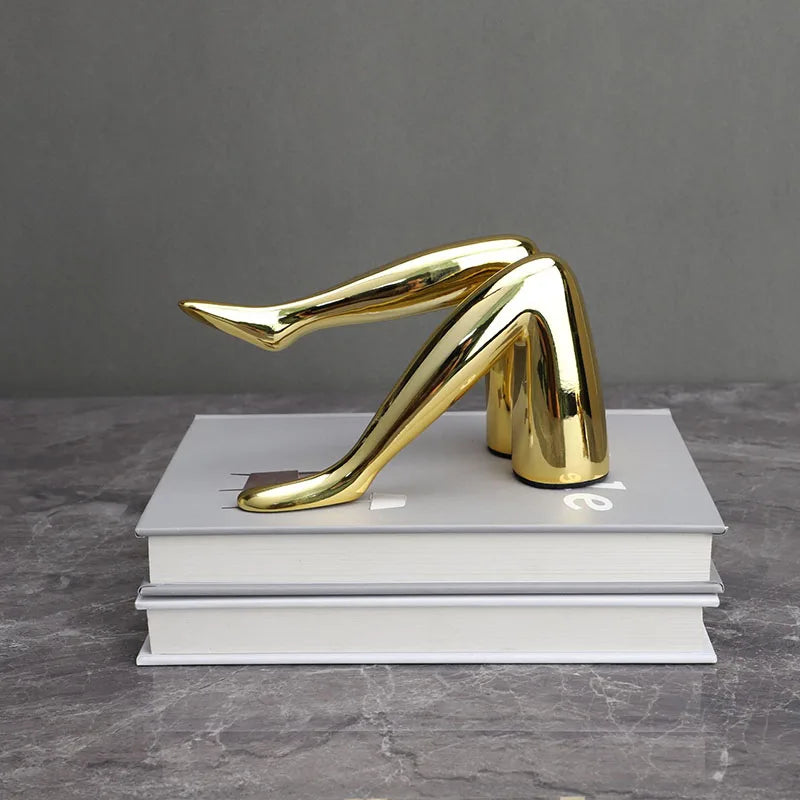 A gold faux finish sculpture of a human leg, cast in resin and displayed on a stack of white books.