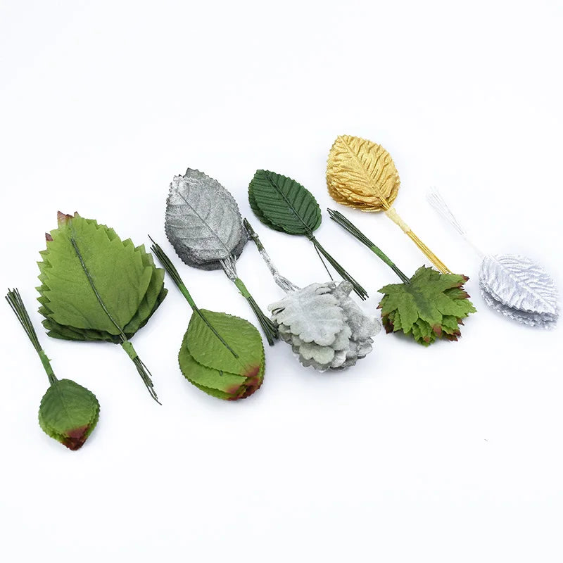 A collection of twelve silk leaf artificial plant stems in various shades of green and gray, some attached to thin gold or si
