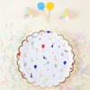 A white paper plate decorated with colorful dots, stars, and small paper party items on a light background.