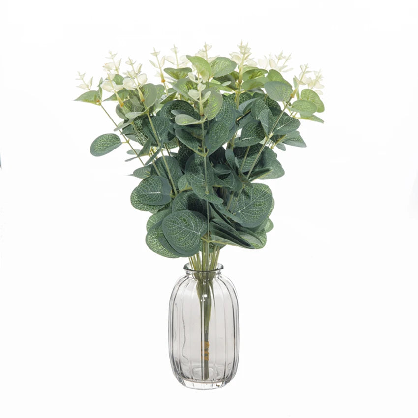 A bouquet of green eucalyptus leaves with small white flowers in a clear glass vase.