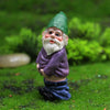 A miniature resin gnome statue with a green hat and white beard sitting in green grass.