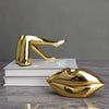 A gold faux finish sculpture of a human face or lips, displayed on stacked white books.