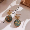 A pair of gold-toned earrings featuring round turquoise stones with gold foil flakes and star-shaped accents.