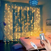 A hand holds a remote control next to warm white LED curtain lights illuminating a window in a bedroom.