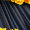 A close-up of bright yellow roses and sunflowers arranged against a dark blue draped fabric.